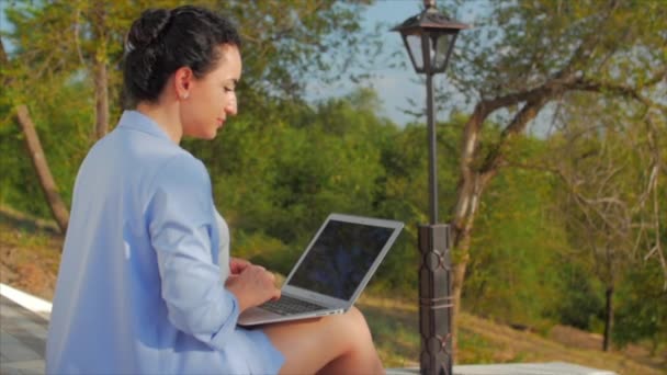Biznes Lady praca na laptopie, atrakcyjna brunetka w niebieskim garniturze z laptopem, atrakcyjna kobieta pracuje na swoim komputerze na zewnątrz. — Wideo stockowe