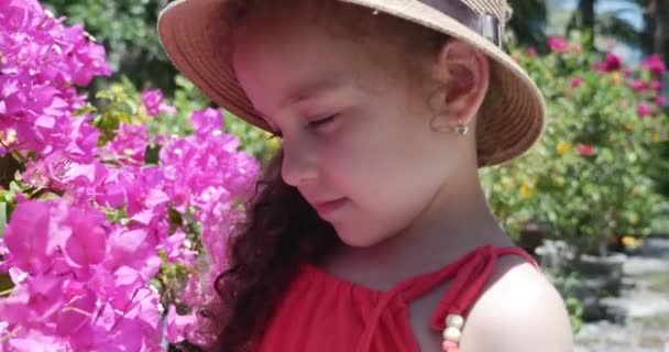 Retrato de menina em um chapéu de palha que está considerando belos botões de flores. Conceito: bebê, criança, crianças, Infância, Verão, liberdade, crianças — Vídeo de Stock