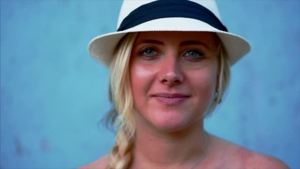 Ritratto di bella donna bionda caucasica in cappello bianco, sorridente alla macchina fotografica. Vista ritagliata, sfondo blu, spazio di copia — Video Stock