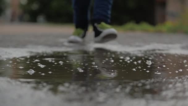 Niños de bajo ángulo, primer plano, irreconocibles corriendo a través de charcos el día de verano después de la lluvia. Los niños despreocupados corren en charcos. Concepto de una infancia feliz . — Vídeos de Stock