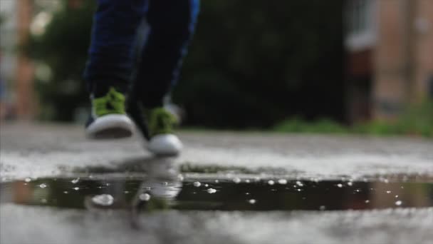 Düşük açı, yakın çekim, tanınmaz çocuklar yağmurdan sonra yaz günü su birikintileri arasında koşuyorlar. Tasasız çocuklar su birikintilerinde koşarlar. Mutlu bir çocukluk kavramı. — Stok video