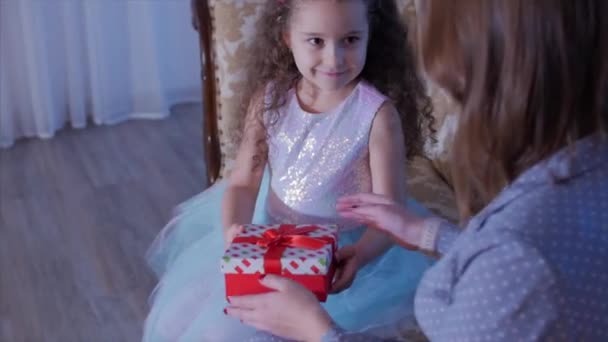 彼女の小さな甘い娘と若い幸せな母親は、贈り物を開き、内側を見て、クリスマスツリーの背景に喜び. — ストック動画