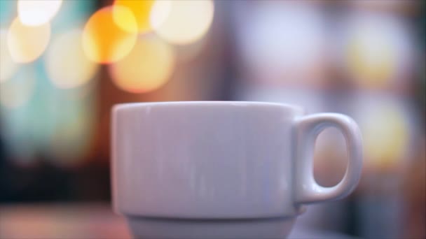 Porseleinen kopje met warme koffie op de achtergrond van lichten in het café. — Stockvideo