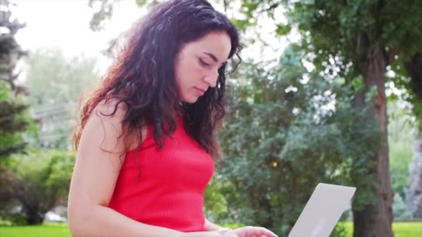 Vrouw werkt op de laptop, aantrekkelijke brunette in een zwarte broek met een laptop werk op het Park, meisje prints op haar computer op buiten. — Stockvideo