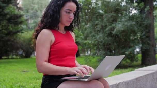Vrouw werkt op de laptop, aantrekkelijke brunette in een zwarte broek met een laptop werk op het Park, meisje prints op haar computer op buiten. — Stockvideo