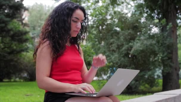 Vrouw werkt op de laptop, aantrekkelijke brunette in een zwarte broek met een laptop werk op het Park, meisje prints op haar computer op buiten. — Stockvideo