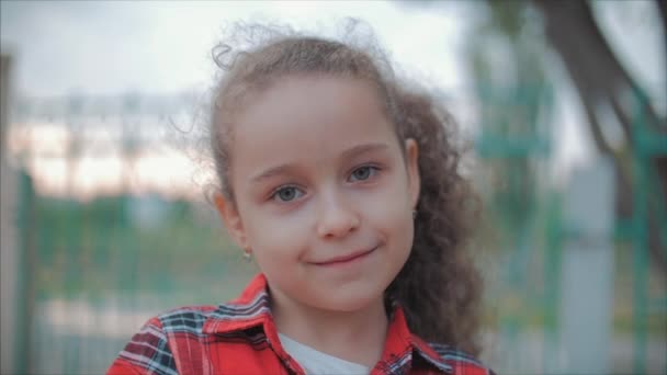 Retrato de cerca de una linda niña caucásica feliz haciendo una cara sorprendida y luego sonriendo mirando a la cámara disfrutando de un cálido día de verano al atardecer . — Vídeo de stock