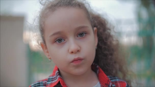 Nahaufnahme Porträt niedliches kaukasisches kleines Mädchen, das in die Kamera schaut und den warmen Sommertag im Sonnenuntergang genießt. — Stockvideo