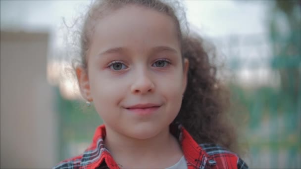 Närbild porträtt av en söt lycklig kaukasiska liten flicka gör en förvånad ansikte och sedan leende tittar på kameran njuter av en varm sommardag vid solnedgången. — Stockvideo