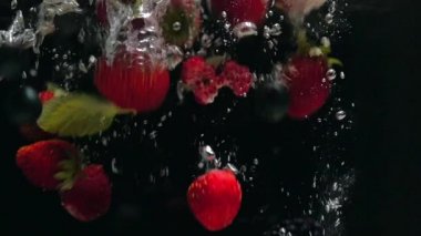 Yaban mersini ve taze nane yaprakları ile Taze ahududu siyah bir arka plan üzerine su içine düşmek, siyah bir arka plan üzerinde sıçrayan. Suya taze meyve ve çilek bırakın. Sağlıklı beslenme, yavaş