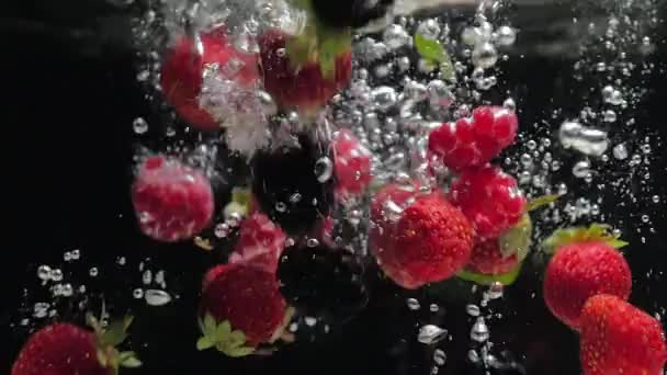 Frambuesas frescas con arándanos y hojas de menta fresca caen sobre un fondo negro en el agua, salpicando sobre un fondo negro. Deje caer frutas y bayas frescas en el agua. Alimentación saludable, lento — Vídeos de Stock