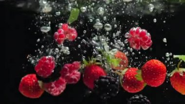 Yaban mersini ve taze nane yaprakları ile Taze ahududu siyah bir arka plan üzerine su içine düşmek, siyah bir arka plan üzerinde sıçrayan. Suya taze meyve ve çilek bırakın. Sağlıklı beslenme, yavaş