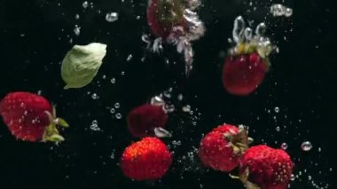 Yaban mersini ve taze nane yaprakları ile Taze ahududu siyah bir arka plan üzerine su içine düşmek, siyah bir arka plan üzerinde sıçrayan. Suya taze meyve ve çilek bırakın. Sağlıklı beslenme, yavaş