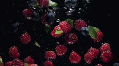 Yaban mersini ve taze nane yaprakları ile Taze ahududu siyah bir arka plan üzerine su içine düşmek, siyah bir arka plan üzerinde sıçrayan. Suya taze meyve ve çilek bırakın. Sağlıklı beslenme, yavaş