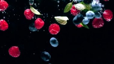 Yaban mersini ve taze nane yaprakları ile Taze ahududu siyah bir arka plan üzerine su içine düşmek, siyah bir arka plan üzerinde sıçrayan. Suya taze meyve ve çilek bırakın. Sağlıklı beslenme, yavaş