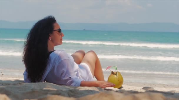 Junge Frau oder ein fröhliches Mädchen, am Strand sonnenbaden, das Meer genießen, Kokosnuss in der Sonne trinken, sich am tropischen Strand entspannen. Konzept des Reisens, Meereswellen, Erholung auf dem Meer im Sommer. — Stockvideo