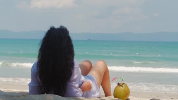 Joven o una chica alegre, tomando el sol en la playa, disfrutando del océano, bebiendo coco al sol, relajándose en una playa tropical. Concepto de viaje, olas del mar, descanso en el mar en el verano . — Vídeo de stock