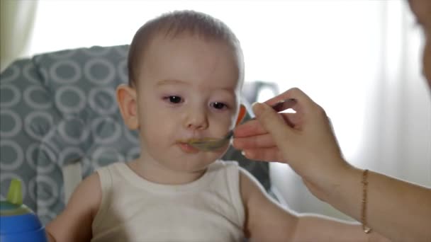 Moeder geeft babyvoeding van een baby lepel, een kind eet vrijwillig. Schattige kleine baby eten haar diner. 4k. — Stockvideo