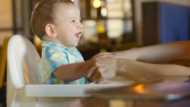 Mamma si pulisce la bocca e le mani al bambino adorabile. Un bambino affascinante ride e applaude. Carino il bambino che mangia la sua cena. 4k . — Video Stock