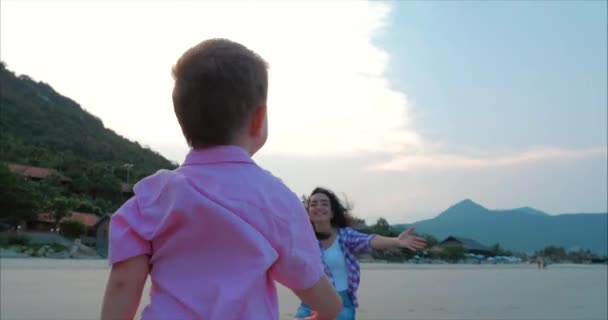 Filho corre para os braços das mães, abraça a mãe. A criança feliz apressa-se em mãos da mãe. Mãe abraços e beijos filho. Abraços familiares sobre o pôr do sol céu fundo . — Vídeo de Stock