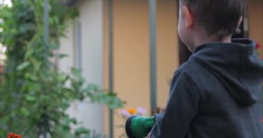 Sprey tabancasıyla çiçekleri sulandıran mutlu küçük bir çocuğun yakın çekim fotoğrafı. Çocuk gülümsüyor, çocuk maceraları kavramı .