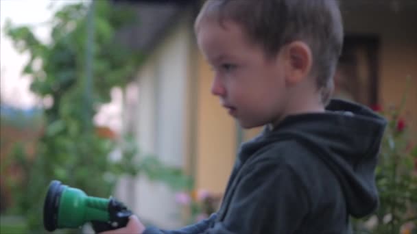 Un primo piano di un bambino felice che innaffia fiori con una pistola a spruzzo. Il bambino sorride, il concetto di avventure per bambini  . — Video Stock