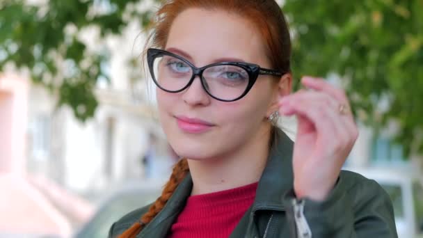 Retrato de una atractiva joven sonriente con gafas cara de cerca de una mujer feliz con el pelo largo y rojo de buen humor, emociones positivas . — Vídeo de stock