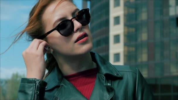 Mujer joven lleva auriculares y enciende música en un teléfono móvil en la calle, mientras camina en un entorno urbano . — Vídeos de Stock