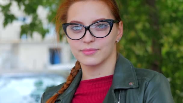 Porträtt av en attraktiv leende ung kvinna med glasögon närbild ansikte en lycklig kvinna med långt rött hår på gott humör, positiva känslor. — Stockvideo