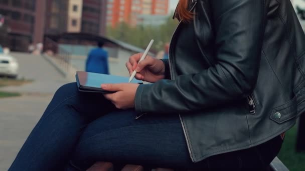 Mujer dibujando en tableta. Chica en el Parque sentado en un banco dibuja en una tableta gráfica . — Vídeos de Stock