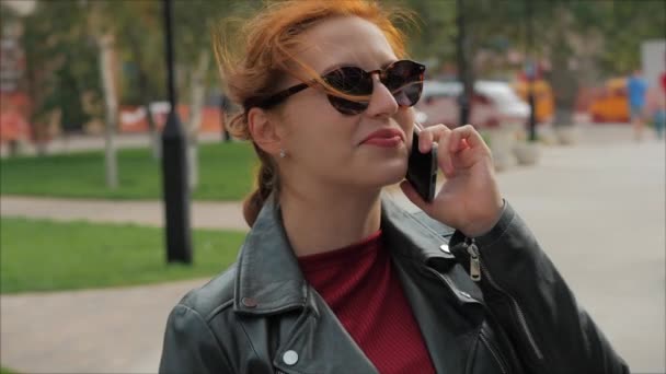 Mujer joven bebiendo café en la calle, escribiendo mensajes de texto en un teléfono móvil, mientras camina en un entorno urbano . — Vídeo de stock