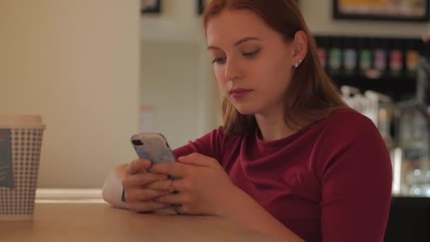 Young woman is sitting in a cafe and typing on a mobile phone. Concept of online stores. — Stock Video
