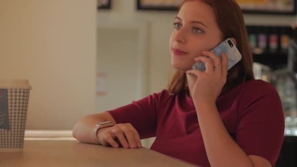 Mujer joven sentada en un café y hablando por teléfono móvil . — Vídeo de stock
