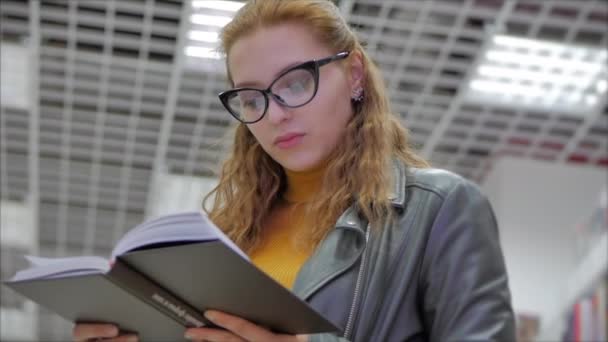 Portret close-up van gelukkig mooi jong vrouw, meisje in glazen student lezen in de bibliotheek universiteit staande in de bibliotheek van de universiteit in de stad. — Stockvideo