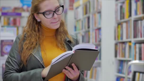 행복하고 예쁜 젊은 여성, 안경을 쓴 학생 이 책 도서관에서 책을 읽고 시에 있는 대학 도서관에 서 있는 모습.. — 비디오