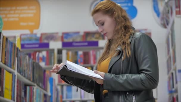 Portrét mladé krásné ženy s jasně červenými vlasy v brýlích, hezká dívka čtení v knihovně University. — Stock video