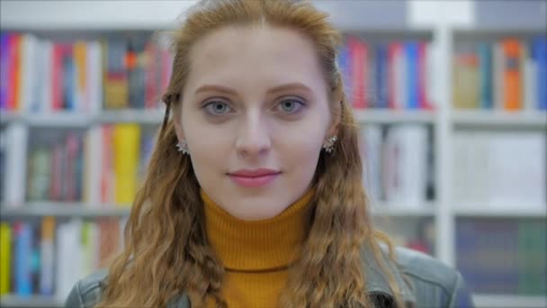 大学図書館に立っているカメラを見て微笑む幸せな若い女性学生の肖像. — ストック動画