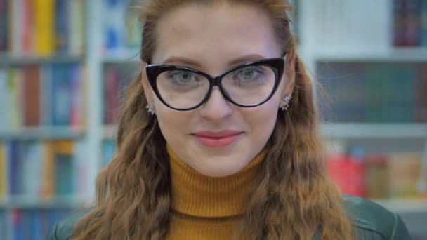 Porträt einer jungen hübschen Frau mit Brille, die in der Bibliothek der Universität in der Stadt ein Buch liest. — Stockvideo