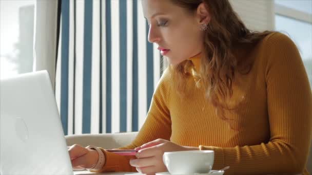 Hermoso día soleado Mujer joven bebe café de la mañana en un café, haciendo en línea un pago fácil de compra en Internet utilizando un teléfono móvil o portátil . — Vídeos de Stock