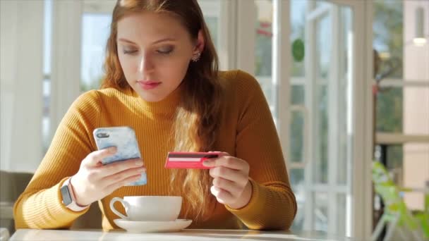 Mooie zonnige dag jonge vrouw drinkt 's morgens koffie in een cafe, het maken van Online een aankoop Gemakkelijke betaling op het internet met behulp van een mobiele telefoon of laptop. — Stockvideo