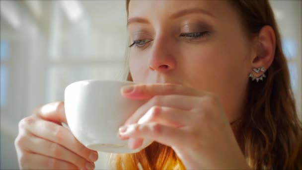 Num dia ensolarado. Closeup Retrato de uma jovem mulher bonita feliz sentada em um café, menina desfrutando de uma xícara perfumada de cappuccino, bebendo seu café da manhã na cidade . — Vídeo de Stock