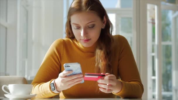 Hermoso día soleado Mujer joven bebe café de la mañana en un café, haciendo en línea un pago fácil de compra en Internet utilizando un teléfono móvil o portátil . — Vídeos de Stock