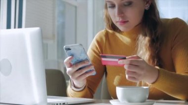 Güzel Gündüz Genç Kadın Bir Kafede Sabah Kahvesini İçiyor, İnternet 'te Cep Telefonu ve Laptop kullanarak İnternetten Kolay Bir Ödeme Yapıyor.
