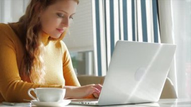 Güzel Gündüz Genç Kadın Bir Kafede Sabah Kahvesini İçiyor, İnternet 'te Cep Telefonu ve Laptop kullanarak İnternetten Kolay Bir Ödeme Yapıyor.