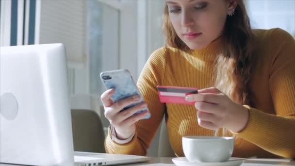 Mooie zonnige dag jonge vrouw drinkt 's morgens koffie in een cafe, het maken van Online een aankoop Gemakkelijke betaling op het internet met behulp van een mobiele telefoon of laptop. — Stockvideo