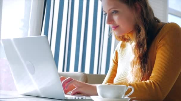 Op een zonnige dag. Portret close-up van gelukkig mooi jong vrouw, meisje zitten in een cafe werken aan een laptop, drinken ochtend koffie in de stad. — Stockvideo