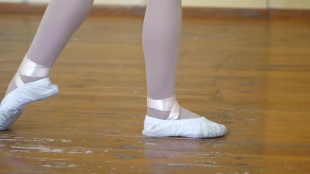 Bale eğitimi sırasında eski bir ahşap zemin üzerinde beyaz bale ayakkabıları kızlar bacaklarda close-up. Klasik dans egzersiz unsuru. — Stok video