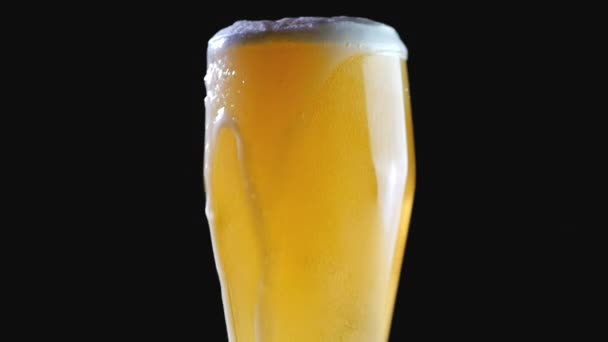Bier wordt op een zwarte achtergrond in het glas gegoten. Schuim glijdt snel door het glas. Extreem groot bierschuim en belletjes. — Stockvideo