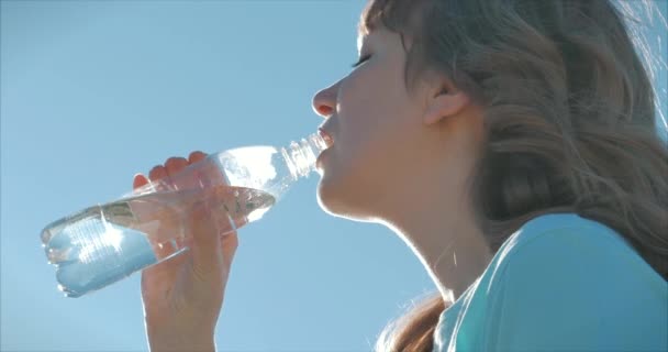 Mulher de aparência europeia ao ar livre bebe água de uma garrafa contra um céu azul claro. Estilo de vida saudável . — Vídeo de Stock