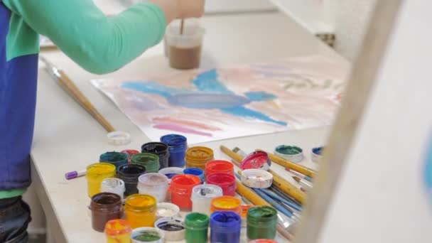Drawing process: in the artists art Studio, hand girl with a brush painting on canvas. Childrens hand of the artist gaining paint on the brush, sitting at the easel in the Studio and draws on canvas — Stock Video